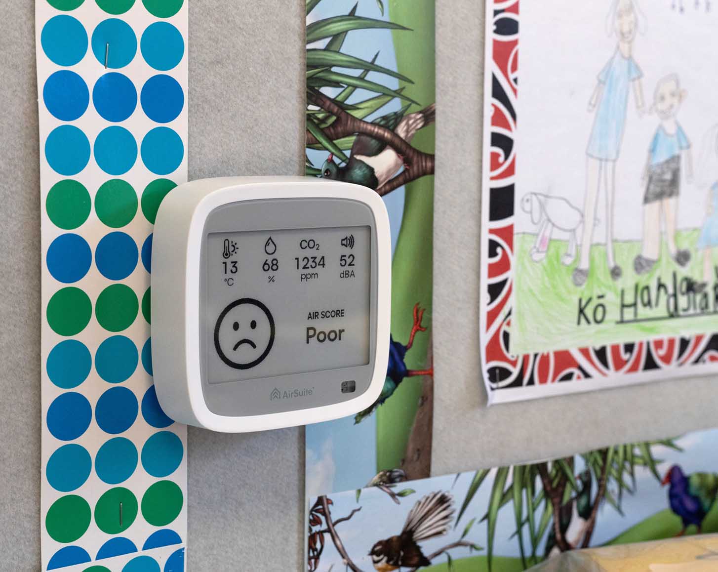 An AirSuite Glance sensor installed on the wall of a classroom, displaying a 'poor' air score