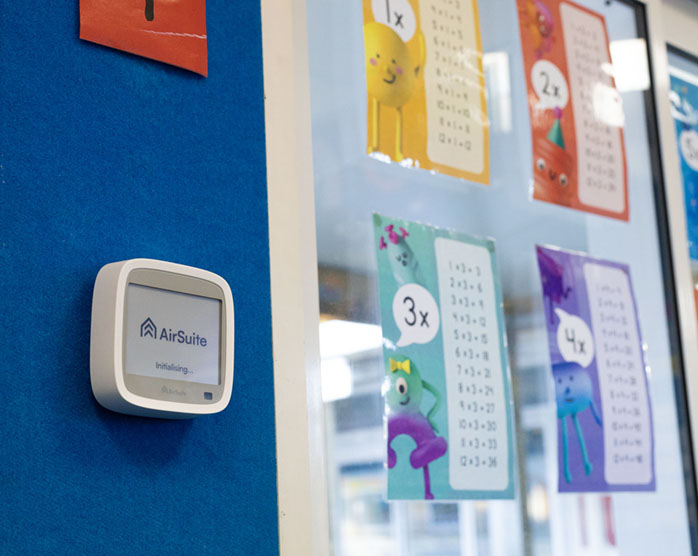 An AirSuite sensor on the wall of a classroom, next to posters of multiplication tables