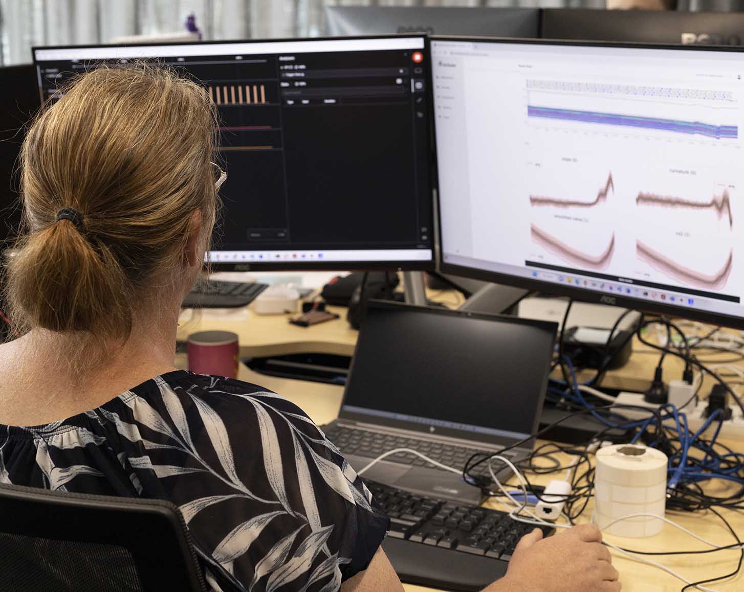A woman looks at data on two computer screens