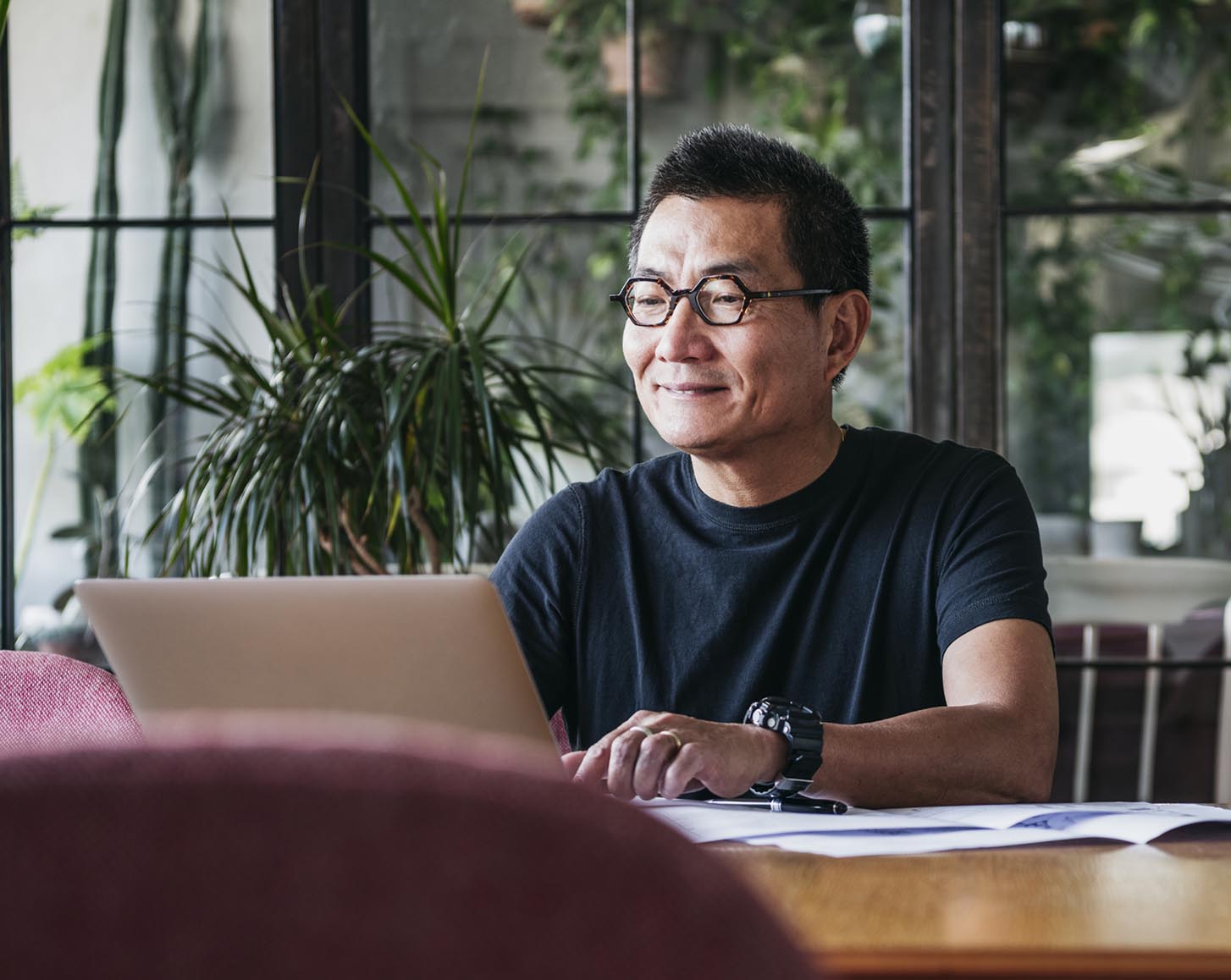 A man with hexagon-shaped glasses using a laptop and smiling