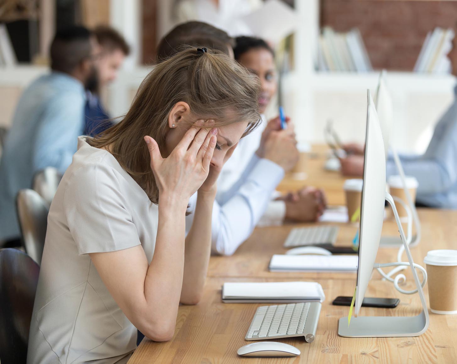 A woman sitting at a computer, rubbing the side of her head