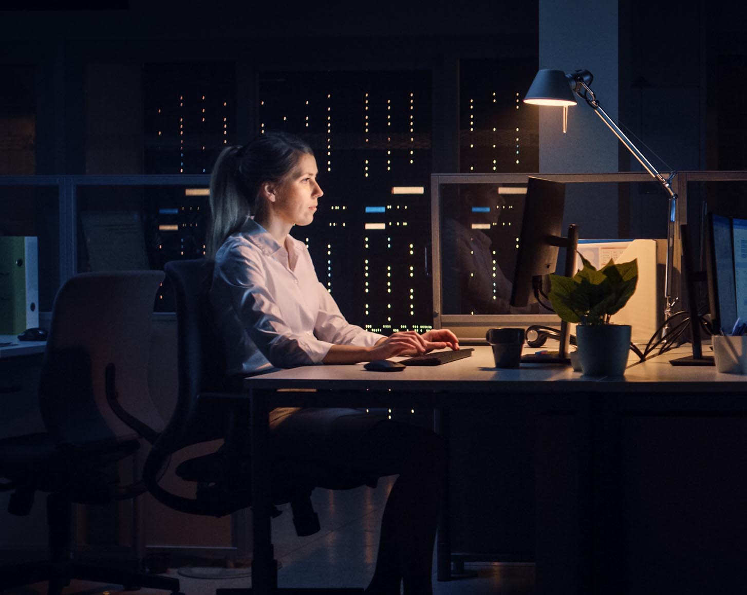 A woman in an office at night, dimly lit by her desk lamp