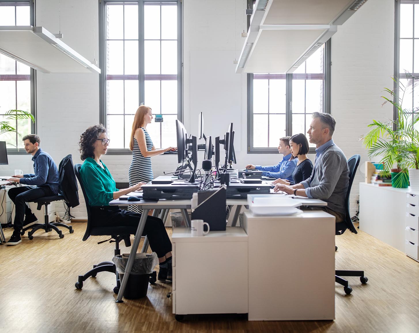 People sitting at their computers, one using a standing desk
