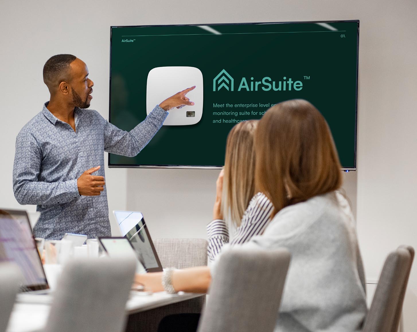 A man pointing to a TV screen and speaking to a presentation about AirSuite sensors