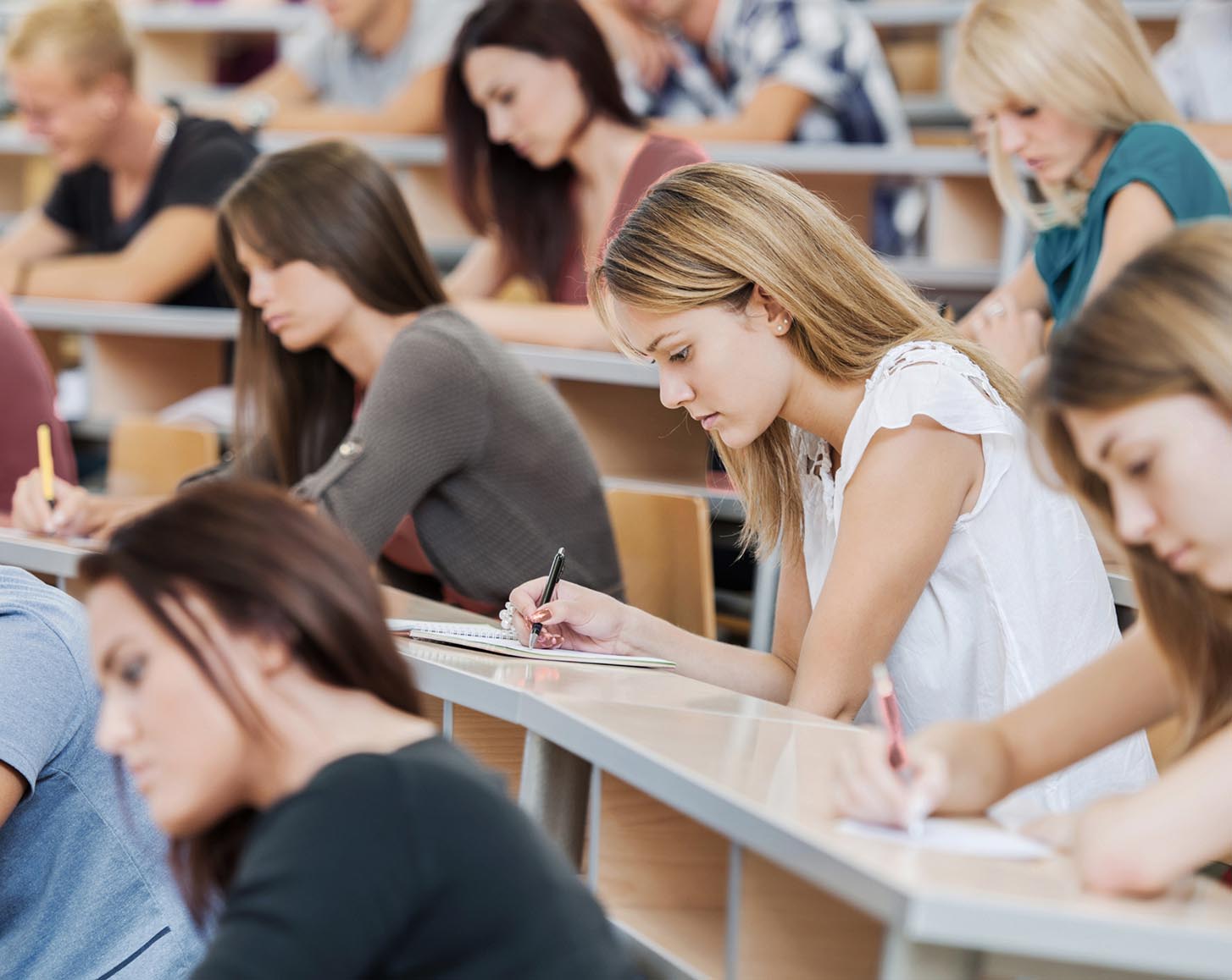 Many university students with their heads down, writing notes