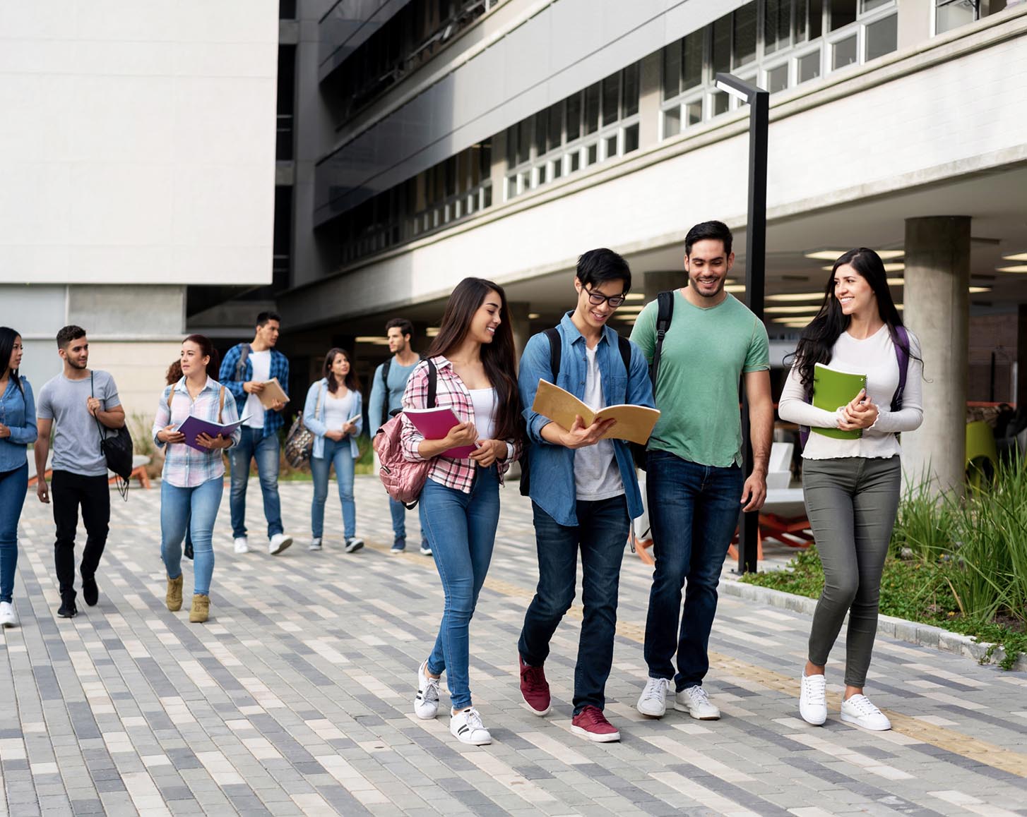 A group of tertiary students holding books, smiling and walking through campus